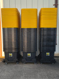 Three stacks of black totes with yellow lids on dollies