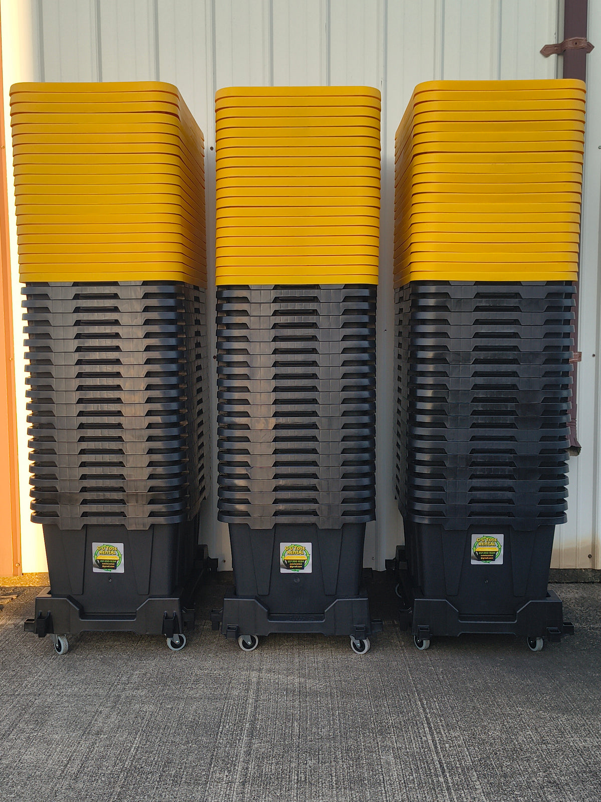 Three stacks of black totes with yellow lids on dollies